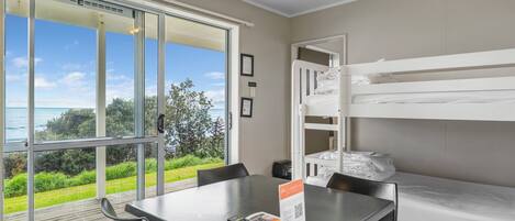 Una habitación con una cama litera, una mesa con un control remoto y vistas al mar a través de amplios ventanales.