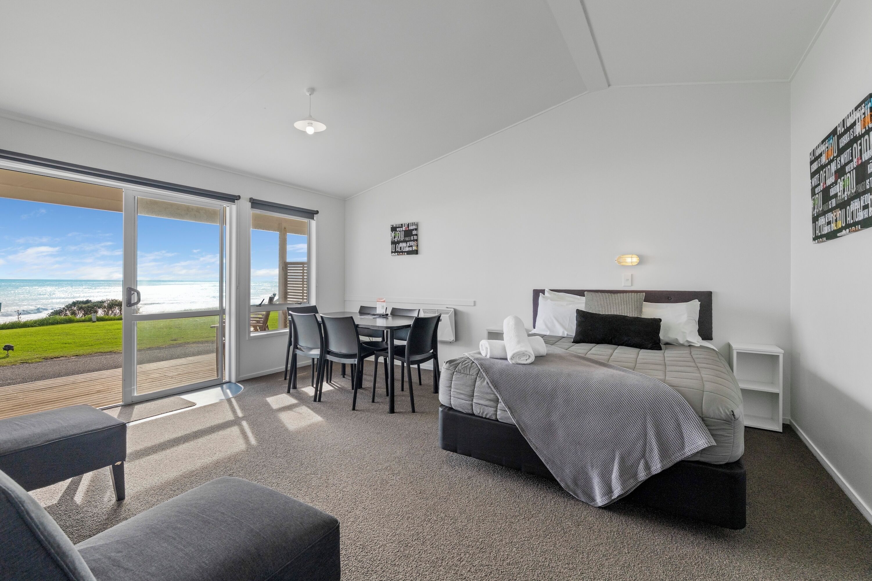 A modern bedroom with a bed, bedside table, and a view of the ocean through large windows.