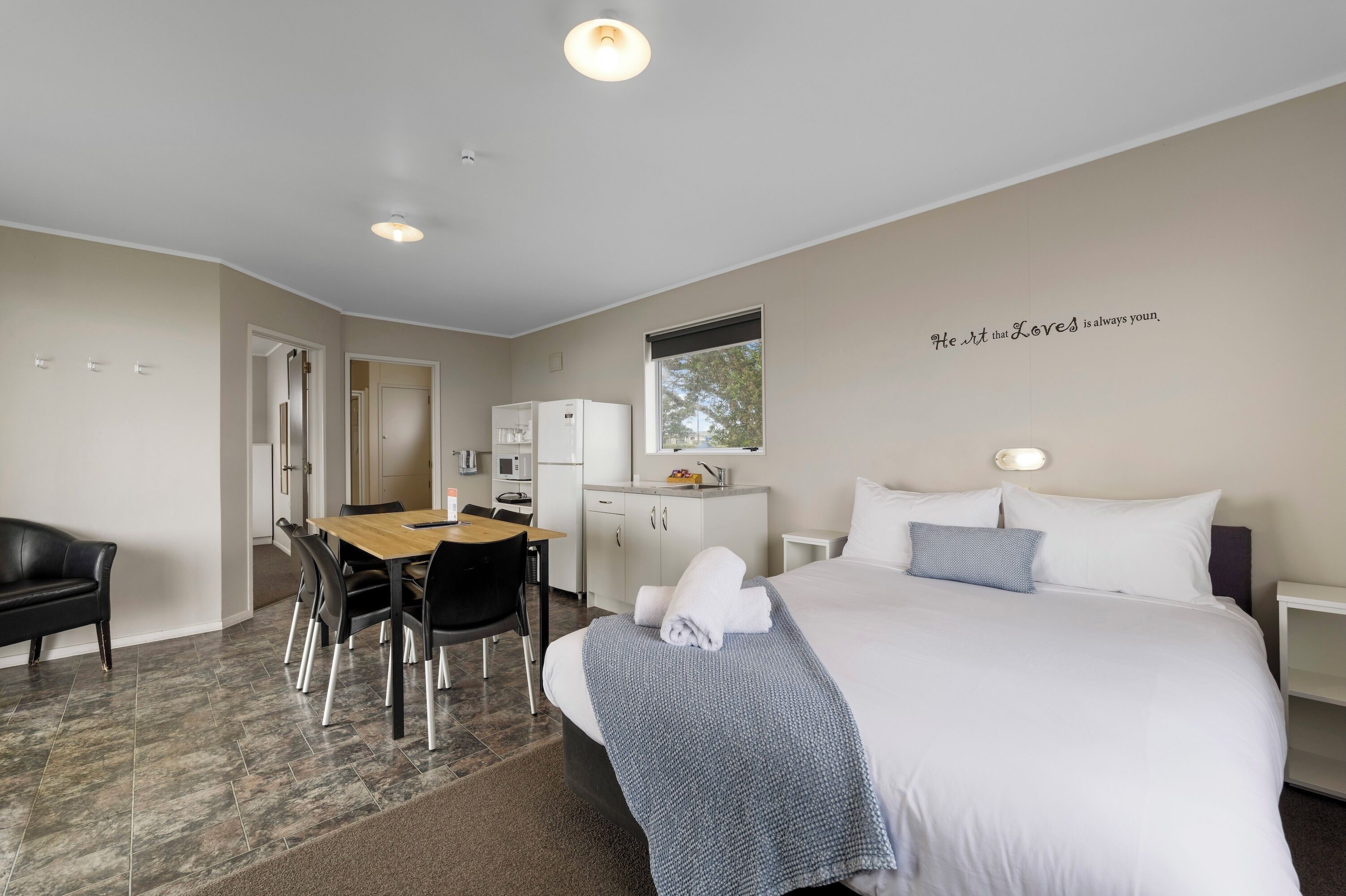 Une chambre d’hôtel avec un lit, un bureau, une chaise, une armoire et une fenêtre.