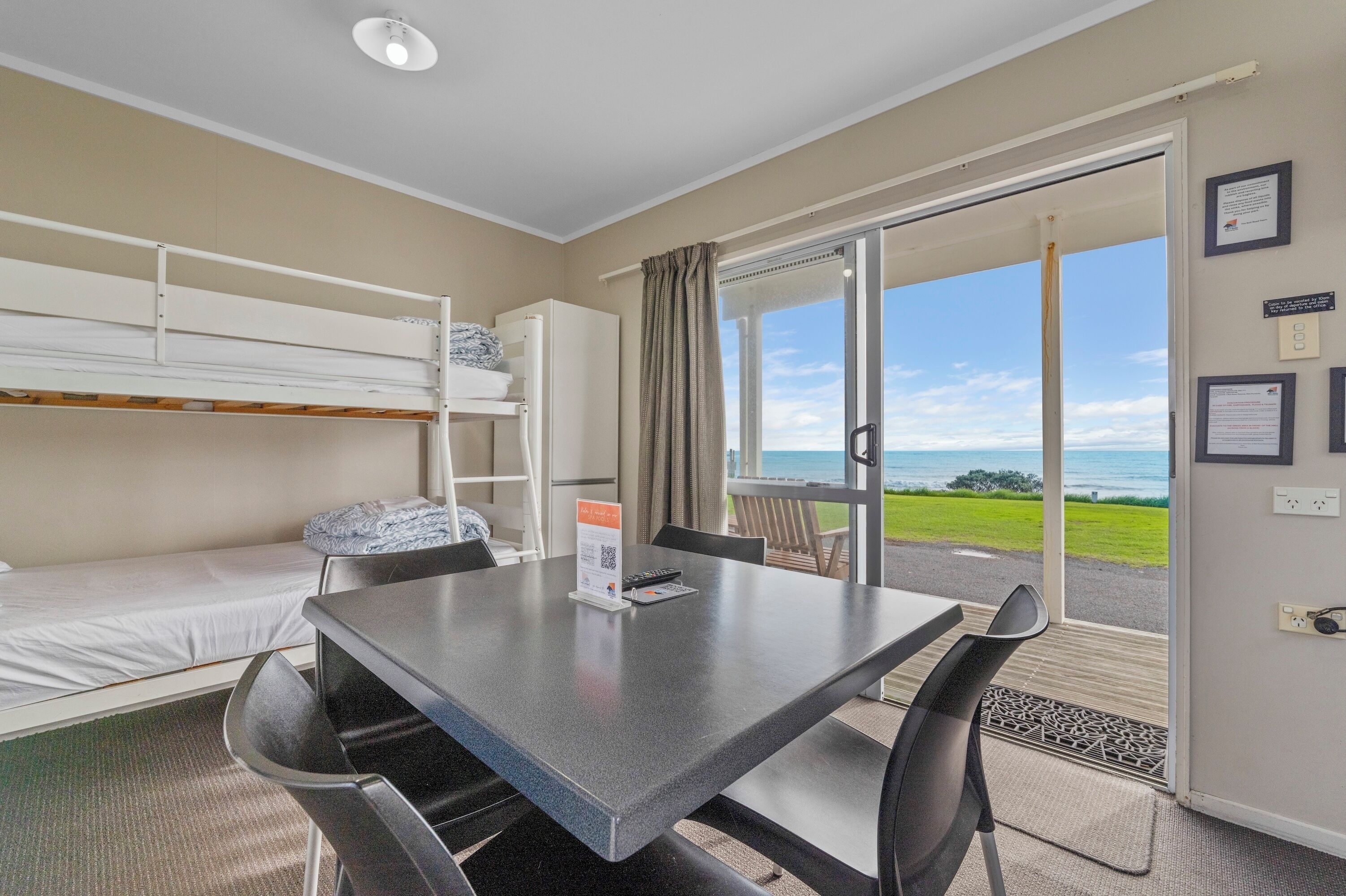 A room with bunk beds, a table with chairs, a view of the ocean, and a door leading outside.