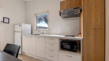 A compact kitchen with white cabinets, a built-in microwave, and a window above the sink.