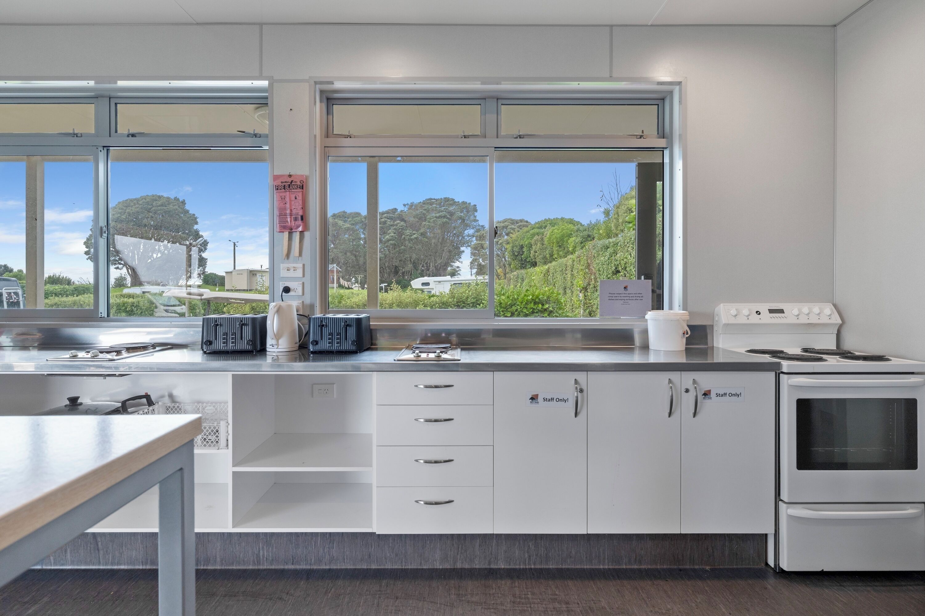 A kitchen with white cabinets, a stove, and a window with a view of trees and a house.