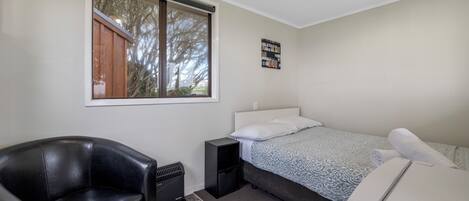 Un dormitorio con una cama, un sillón de cuero negro, un calentador y una ventana con vista a árboles.