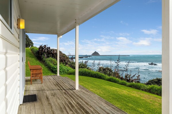 Une terrasse en bois avec un banc, offrant une vue sur la côte, avec une zone herbeuse et un affleurement rocheux au loin.