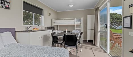 A compact hotel room with a bunk bed, a small kitchenette, a dining area, and a sliding glass door leading to an outdoor deck.