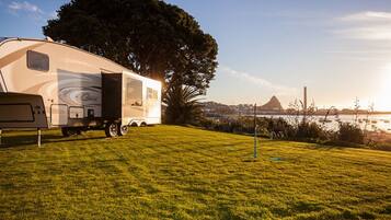 A recreational vehicle parked on a grassy area with a large tree and a view of a distant mountain and water body.