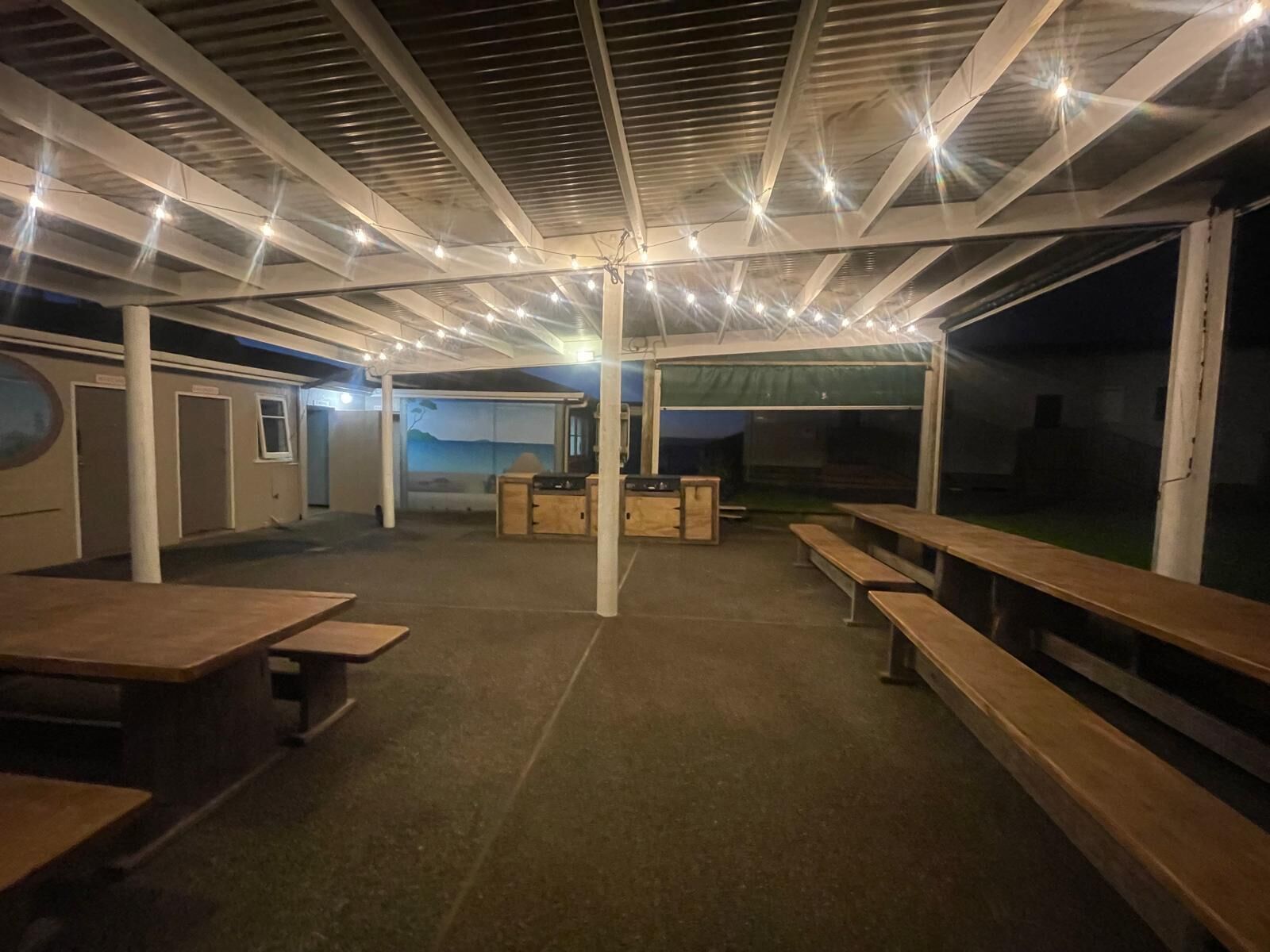 Un espacio al aire libre cubierto con bancos y mesas de madera, una estación de parrilla y vista al mar.