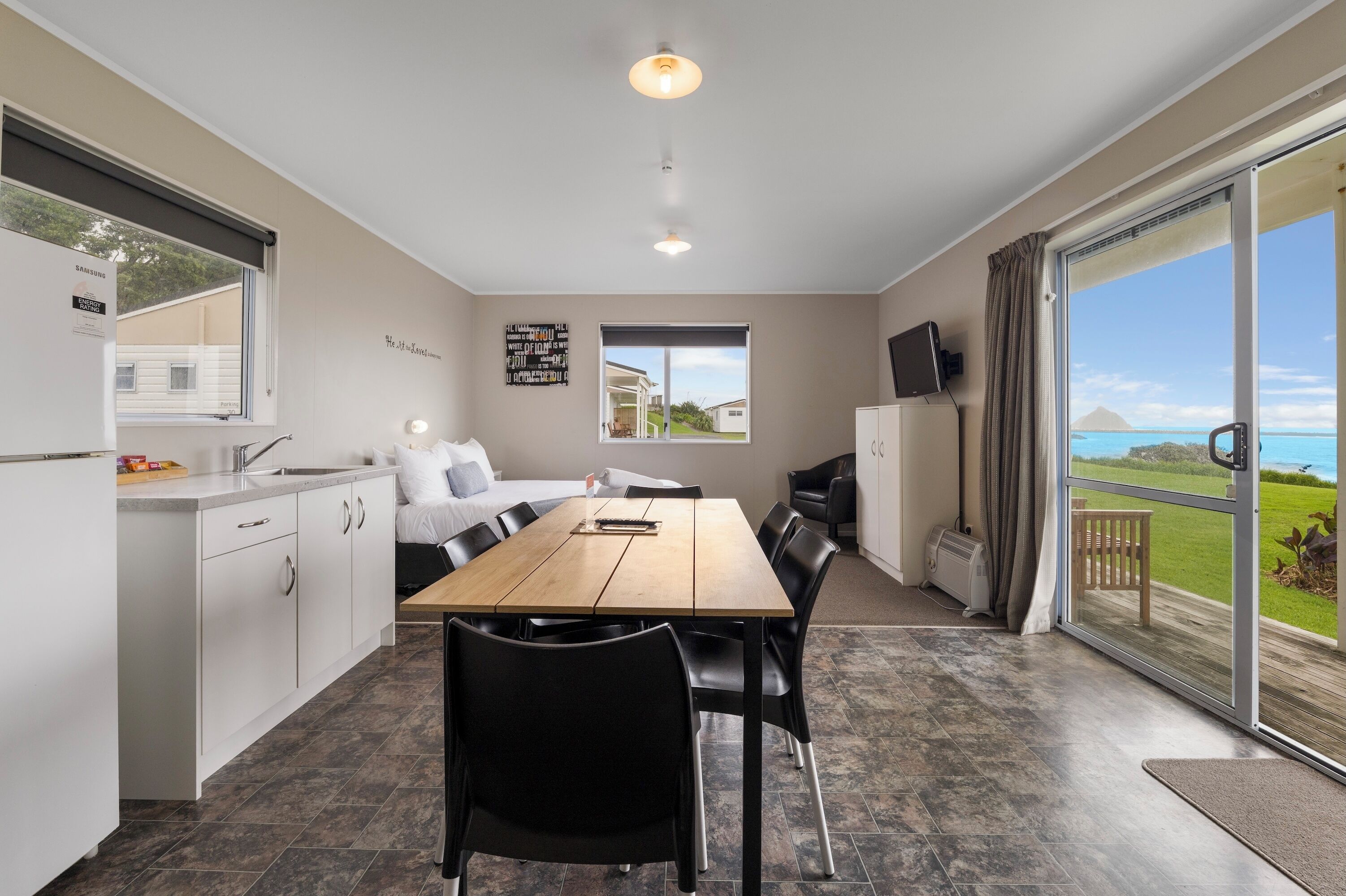 A modern kitchen with a dining area, large windows, and a view of the outdoors.