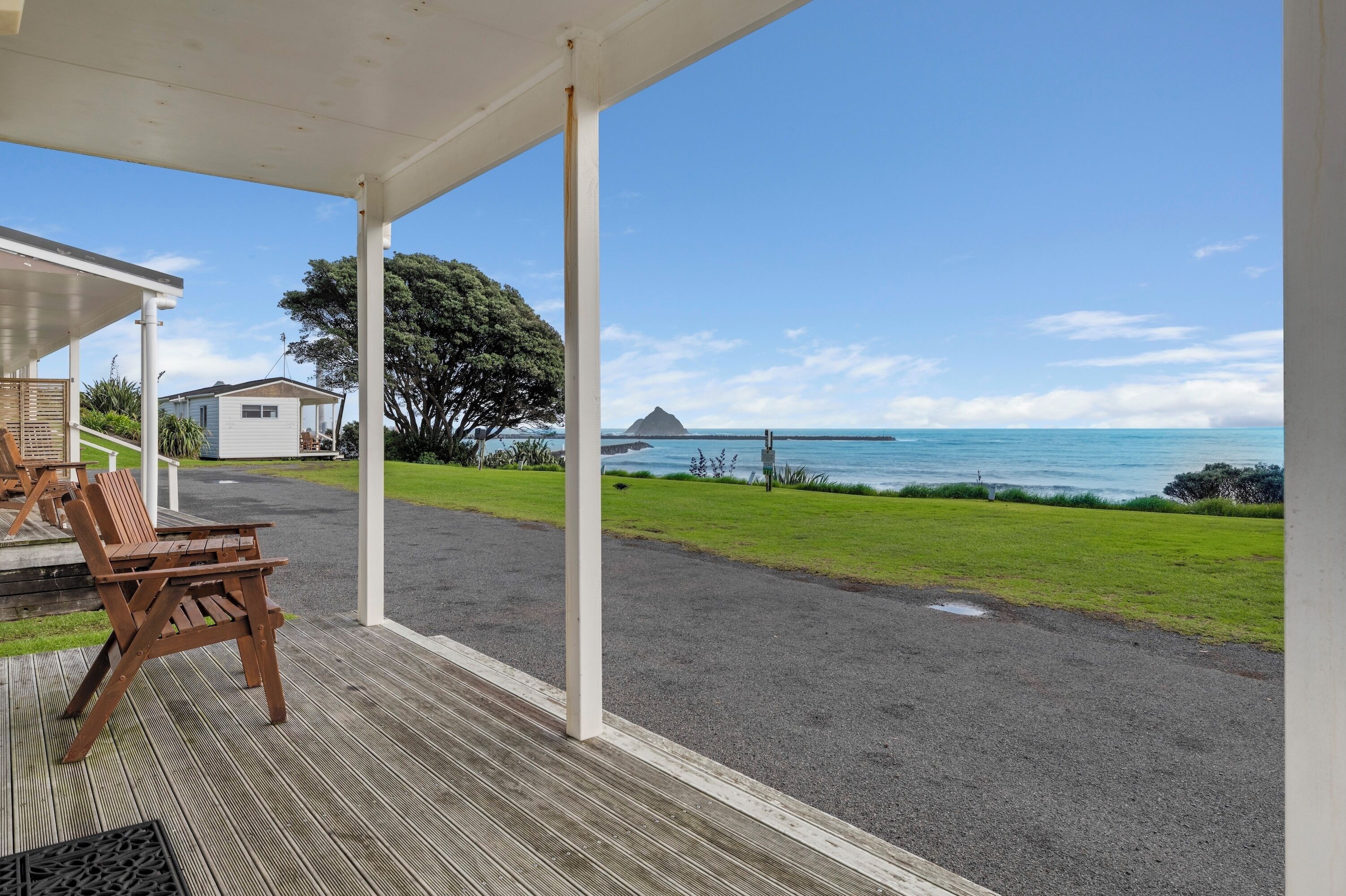 A covered outdoor area with a view of the ocean, a grassy path, and a wooden bench.
