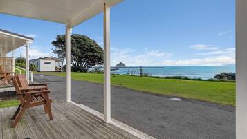 A covered outdoor area with a view of the ocean, a grassy path, and a wooden bench.