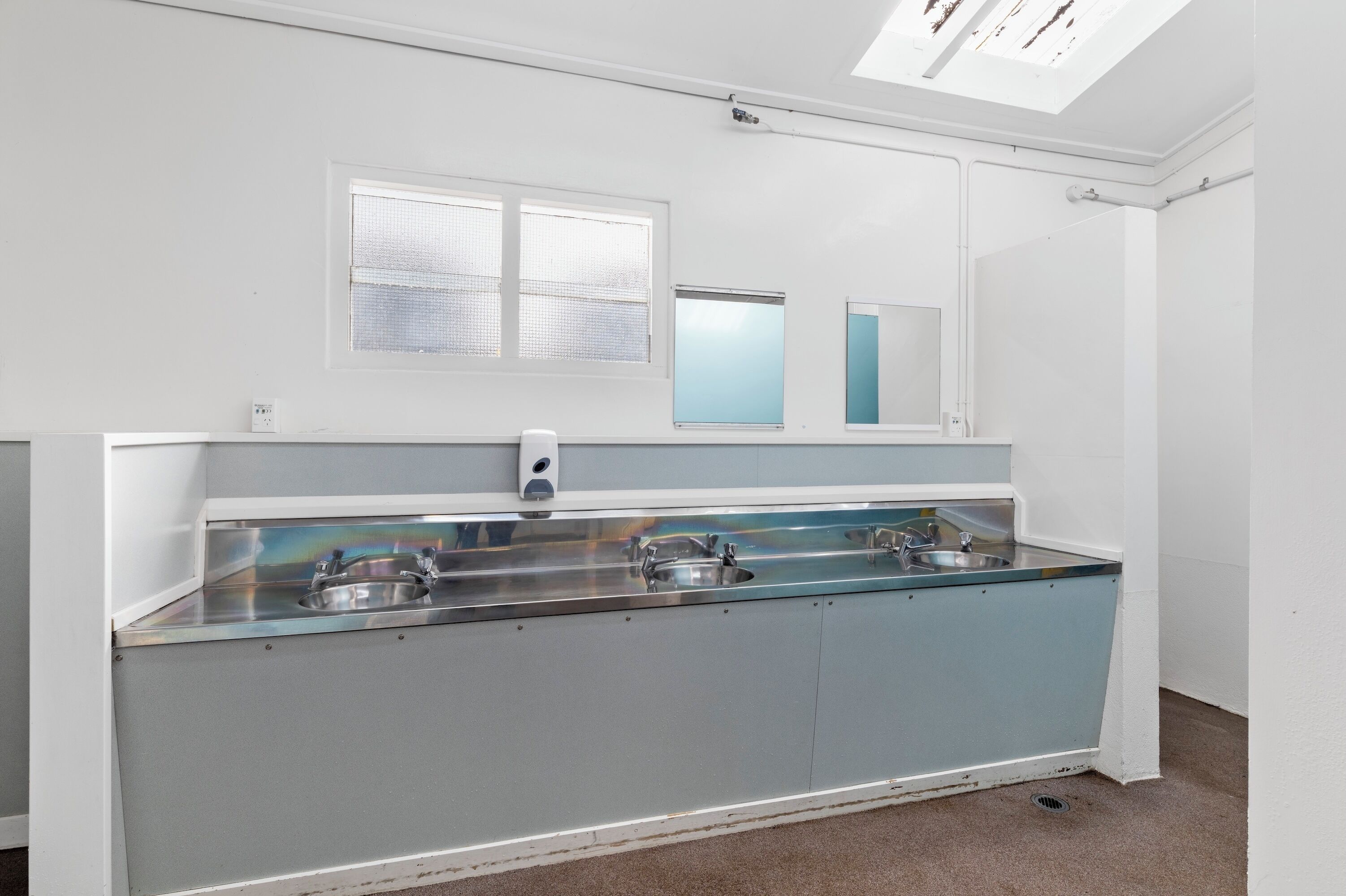 A modern bathroom with a glass-enclosed sink, a mirror, and a skylight.