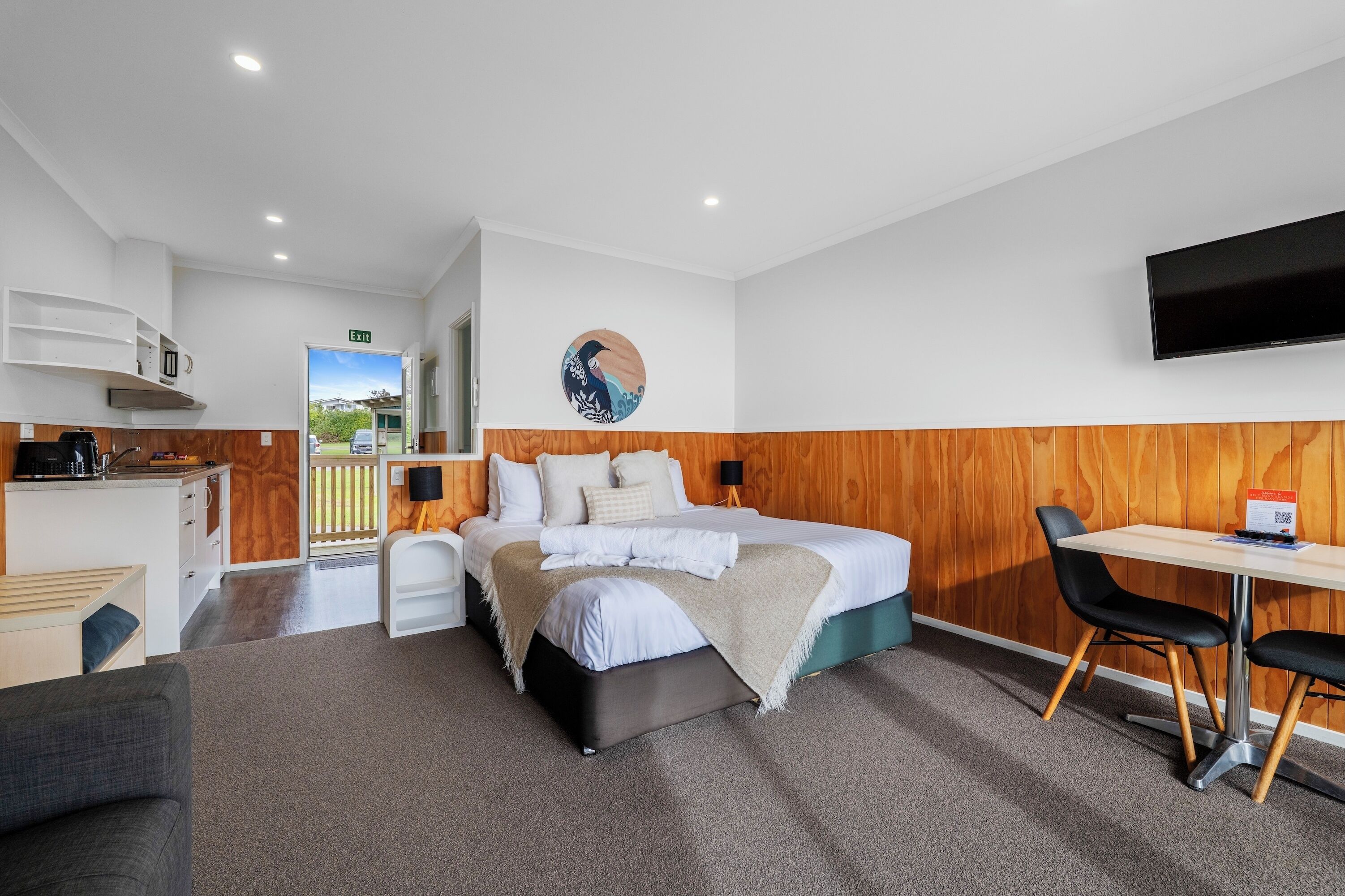 A modern hotel room with a bed, a desk, a chair, a TV, and a view of the outdoors.
