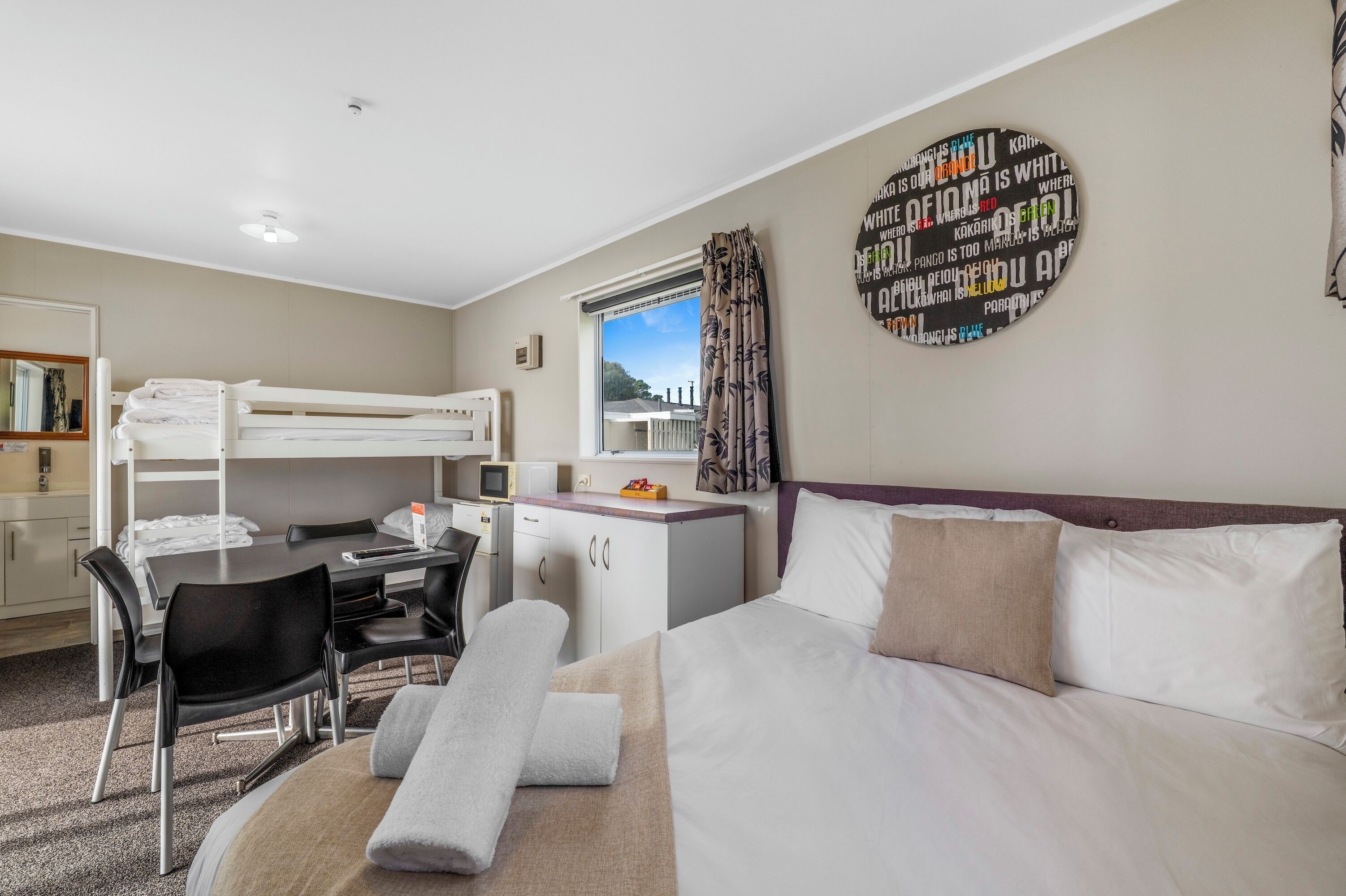 Une chambre d’hôtel avec un lit superposé, un bureau avec une chaise, un petit placard et un lit avec des oreillers.