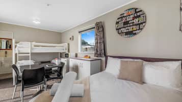 Une chambre d’hôtel avec un lit superposé, un bureau avec une chaise, un petit placard et un lit avec des oreillers.