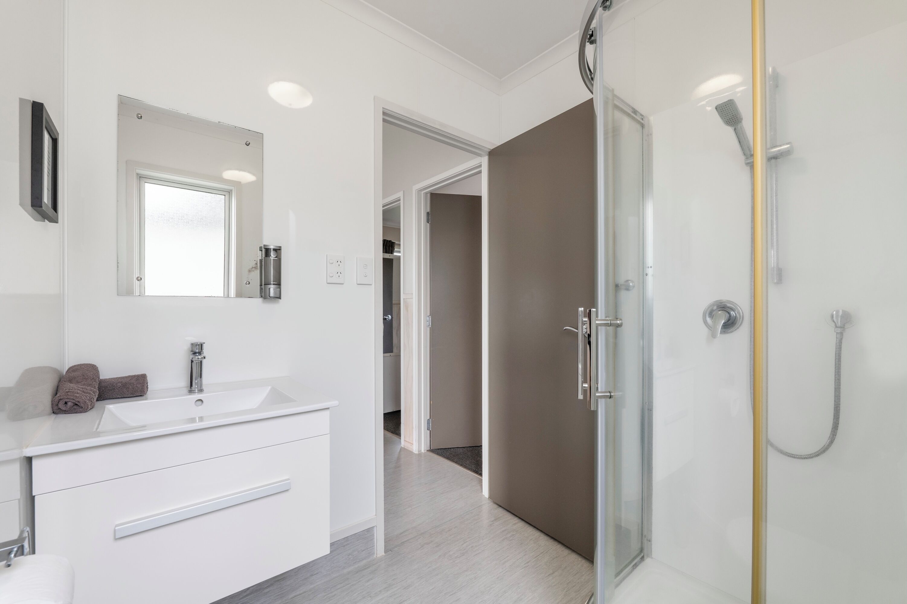 A modern bathroom with a white vanity, a glass shower enclosure, and a visible hallway leading to another room.