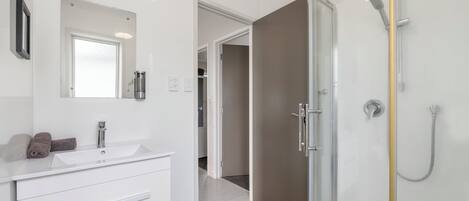 A modern bathroom with a white vanity, a glass shower enclosure, and a visible hallway leading to another room.