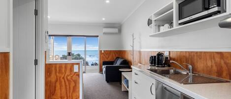 A modern kitchen with a built-in microwave, stainless steel sink, and a dishwasher. There is a wooden accent wall and a view of the ocean through a large window.