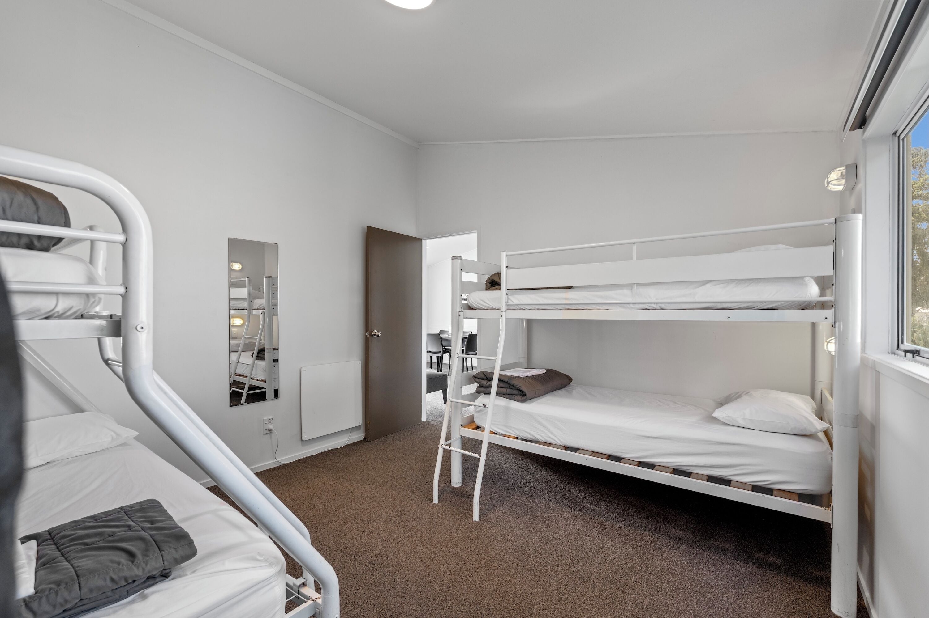 Een slaapkamer met stapelbed, een ladder, een spiegel en een deur naar een andere kamer.