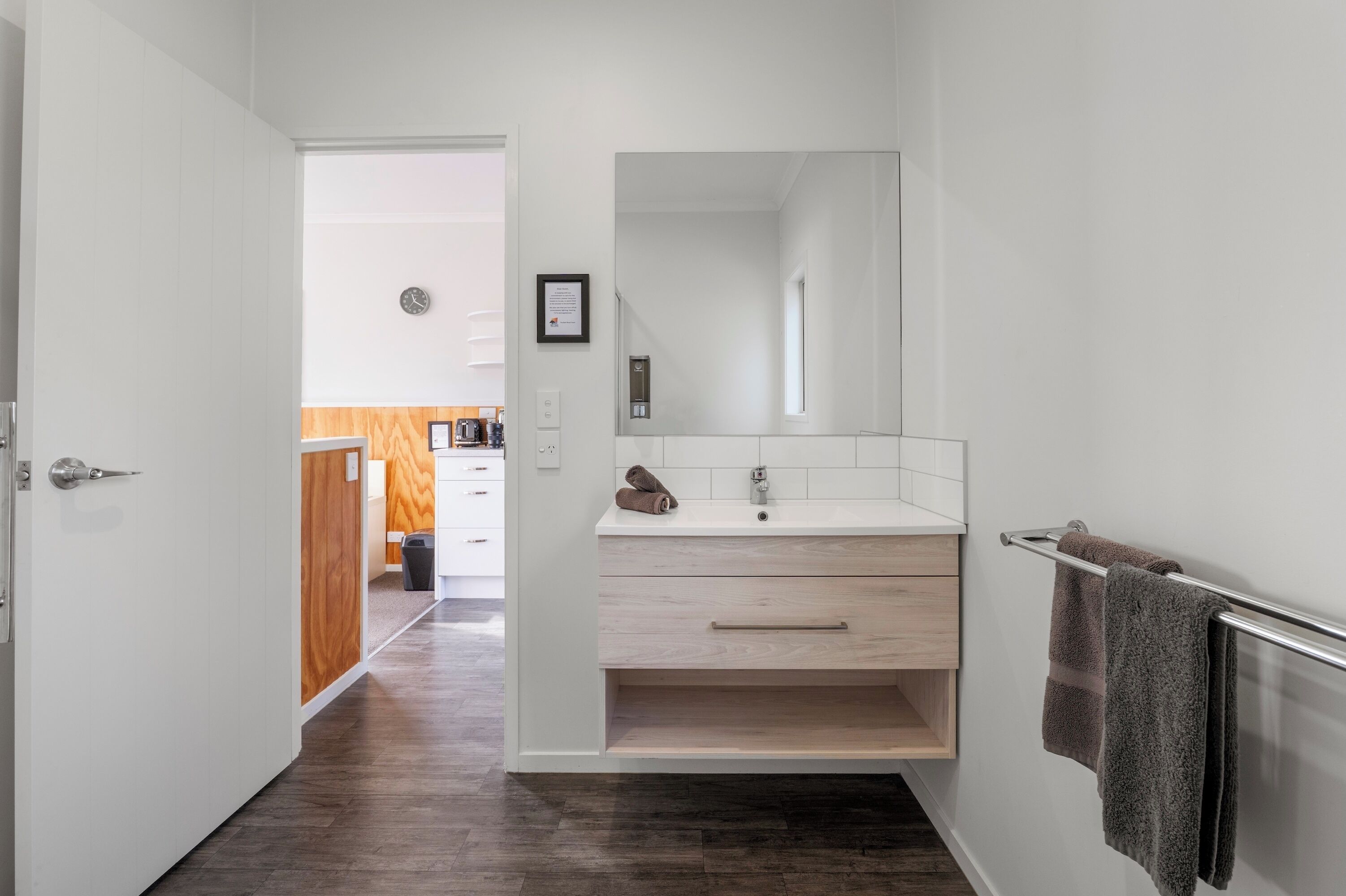 A modern bathroom with a wooden vanity, a large mirror, and a towel rack.