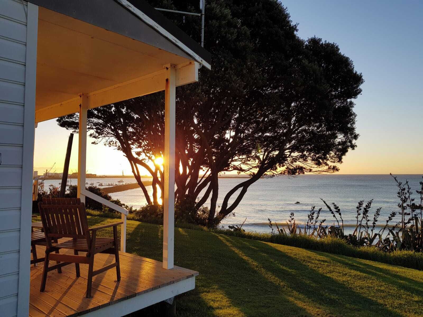 A covered outdoor seating area with a view of the sea and a large tree.