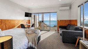 Une chambre d’hôtel moderne dotée d’un grand lit, d’un canapé, d’un bureau et offrant une vue sur l’océan grâce à des portes vitrées.