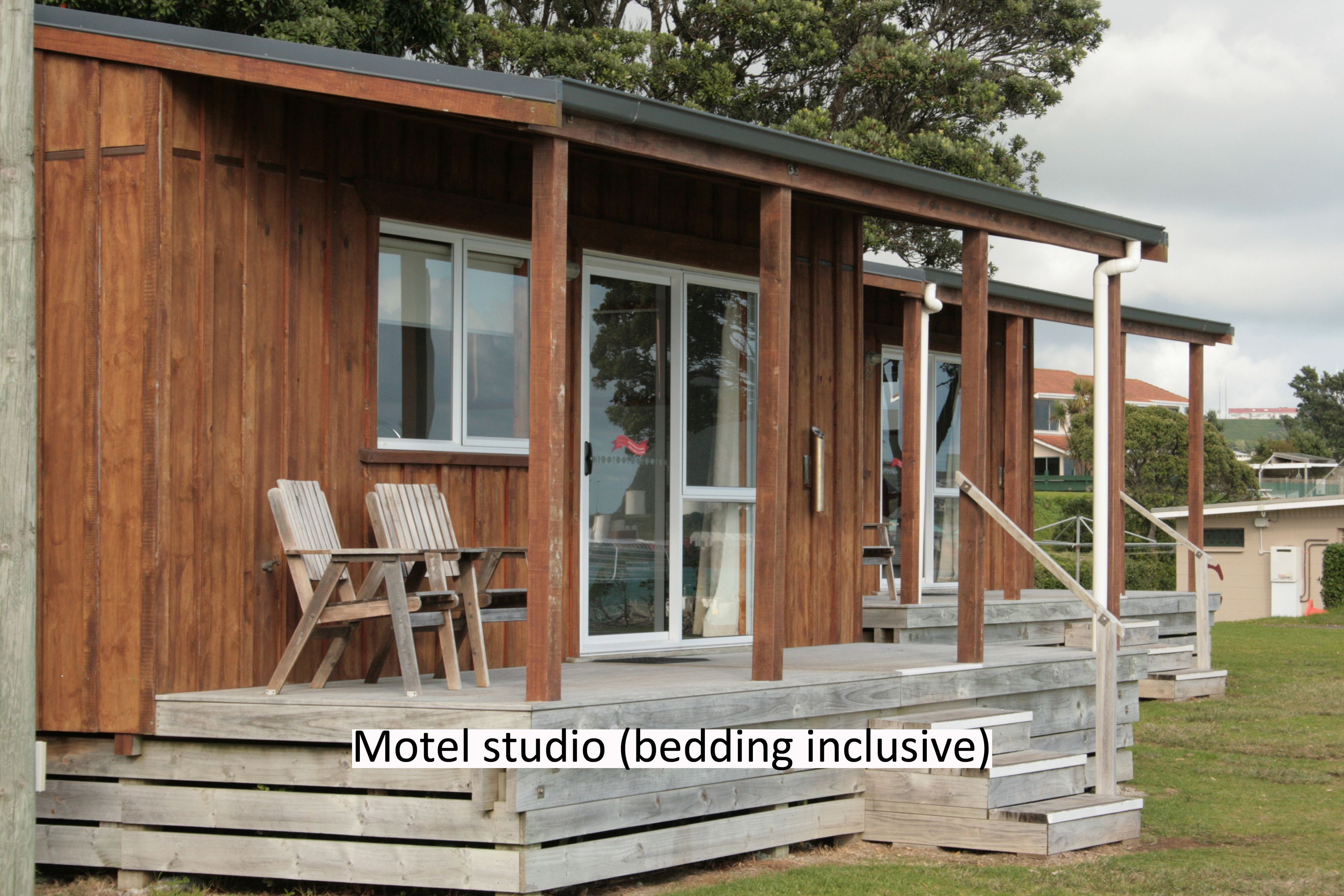 A motel studio with a wooden exterior, a covered porch, and a staircase leading to the entrance.