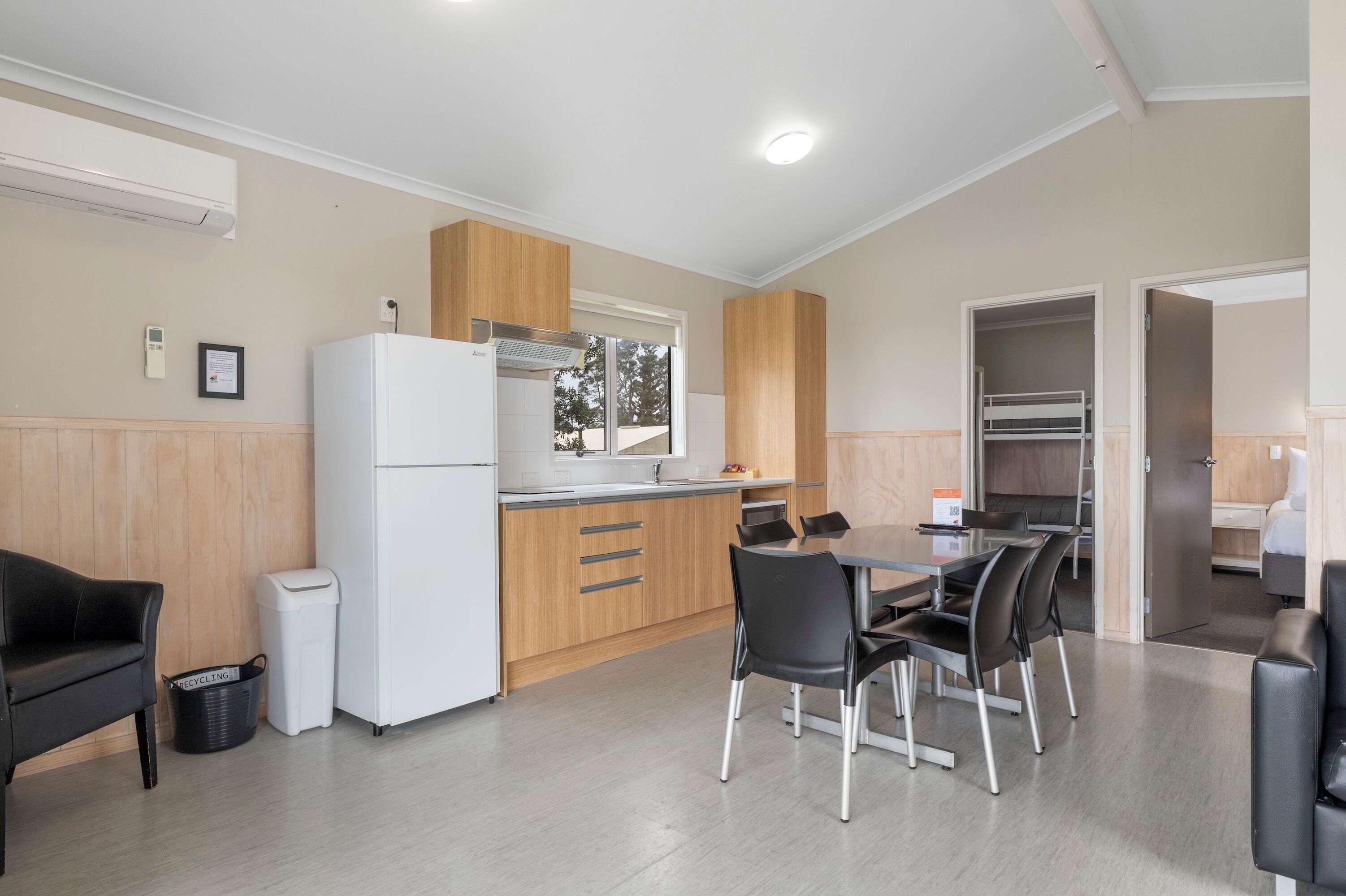 A modern kitchen with a refrigerator, stove, and wooden cabinets. There is a dining table with chairs and a trash bin.