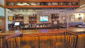 A bar area with wooden bar top, hanging wine glasses, and a television displaying a nature scene. - Nobel Hostel Guesthouse (Istanbul)