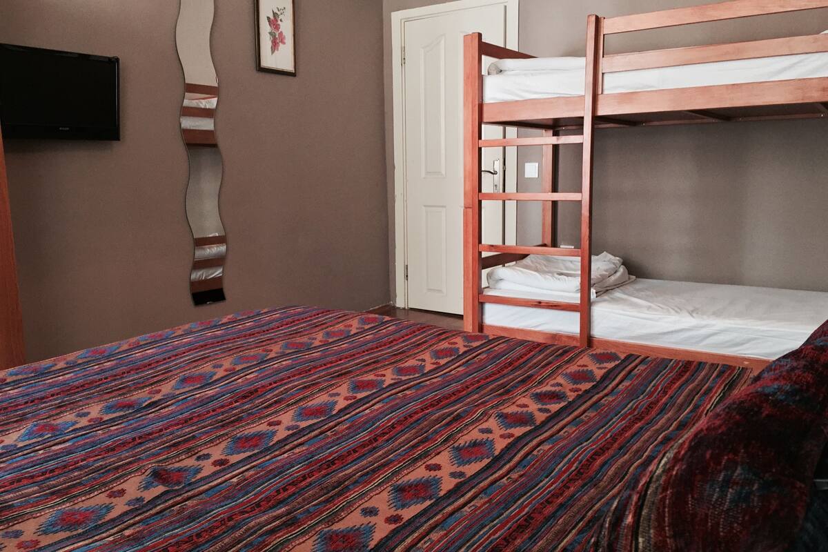 A room with a bunk bed, a patterned carpet, a door, and a flat-screen TV mounted on the wall.