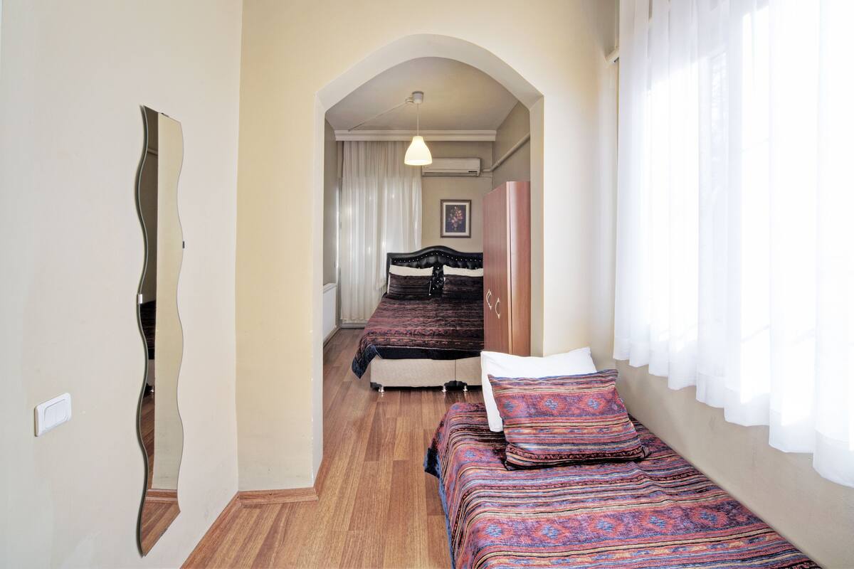 A narrow hallway leading to a bedroom with two beds, a wardrobe, and a hanging light fixture.