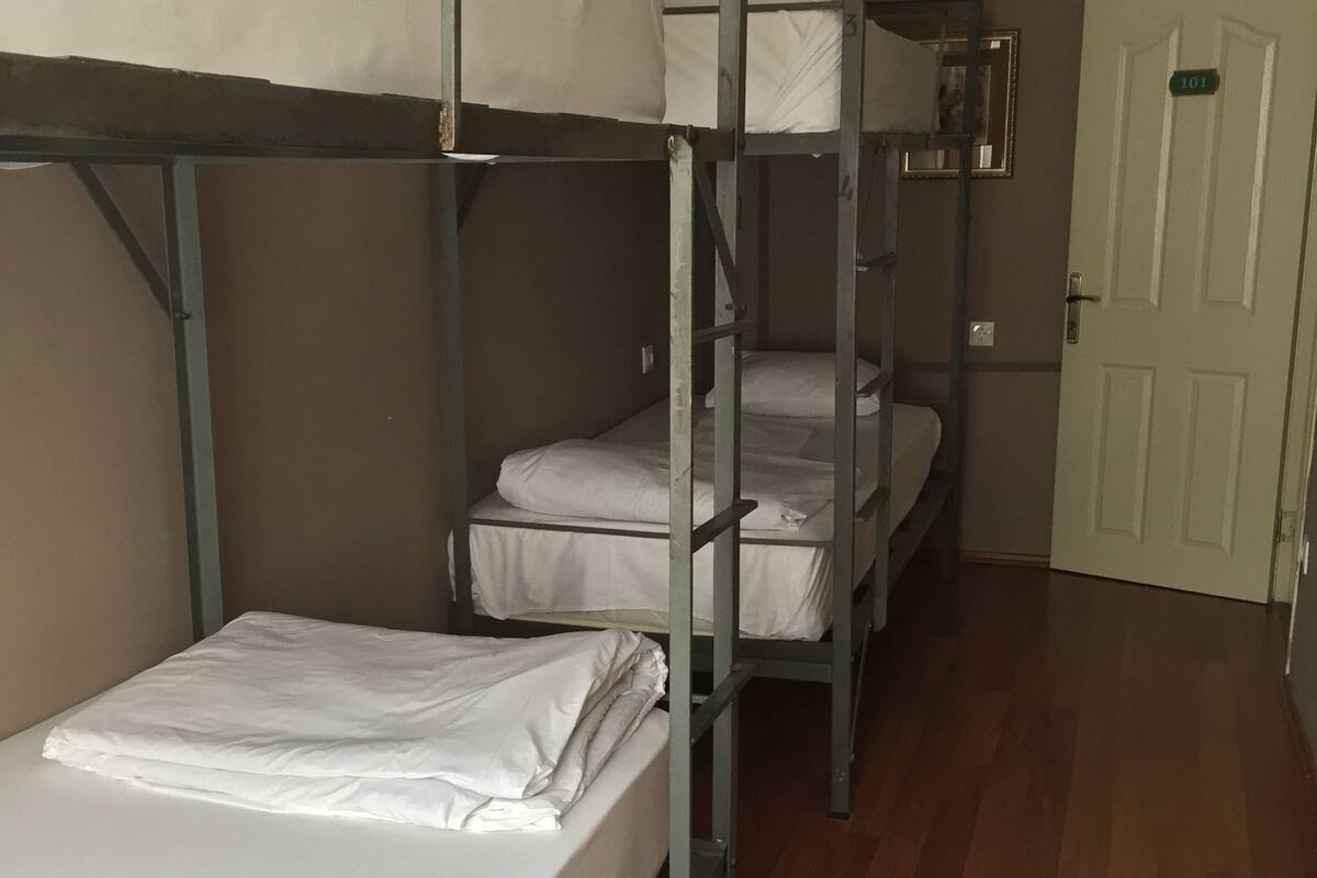 A room with bunk beds, wooden flooring, and a door with a number sign.