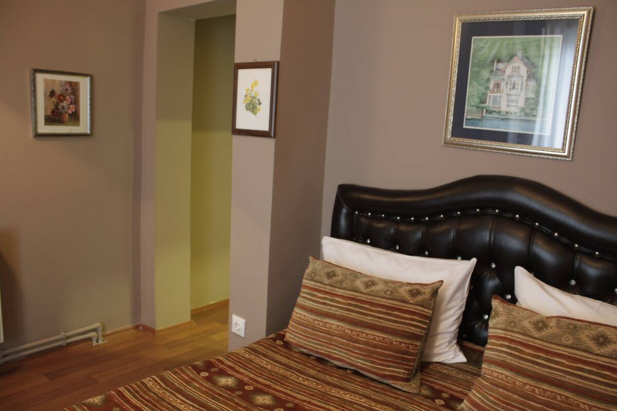 A bedroom with a dark leather headboard, patterned bedding, and framed artwork on the walls.