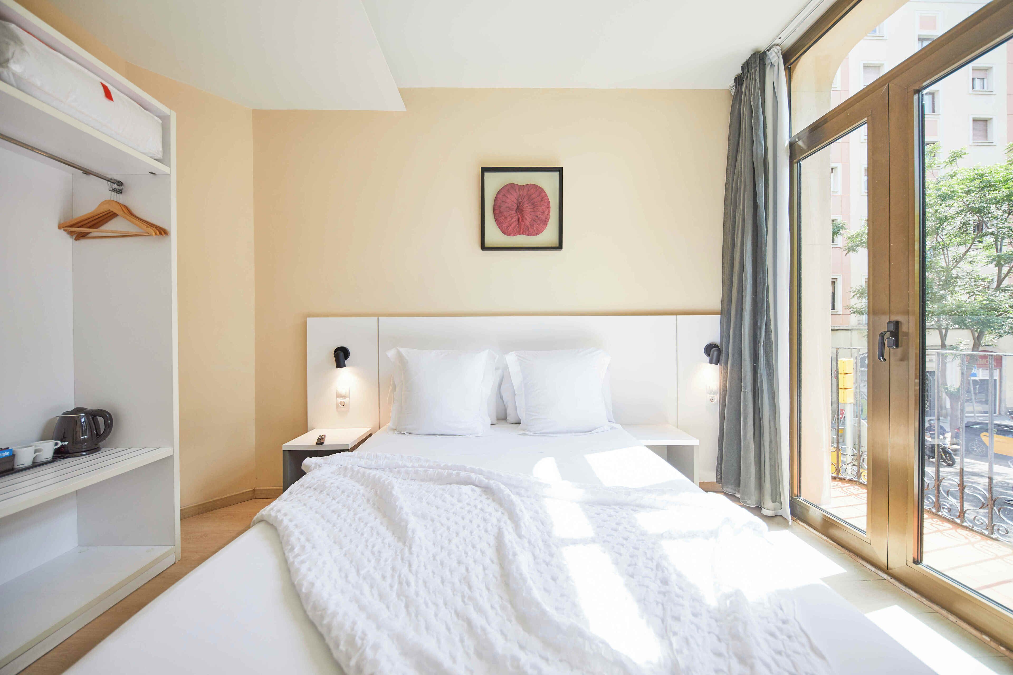 A hotel room with a bed, a wardrobe, a nightstand, a framed picture on the wall, and a view of the outside.
