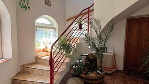 A staircase with a red railing leading to a landing area with a decorative plant arrangement and a wooden cabinet.