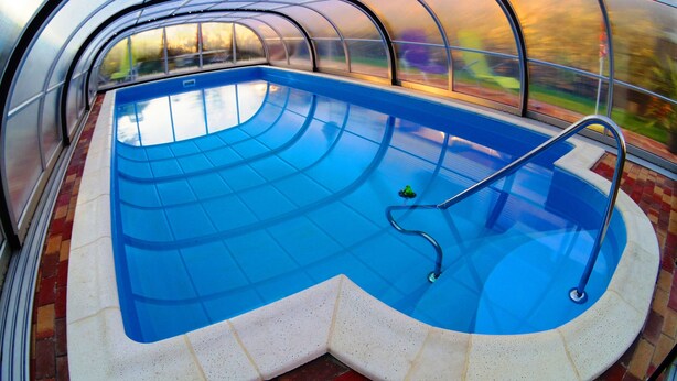 A swimming pool with a glass enclosure, clear blue water, and a brick border.