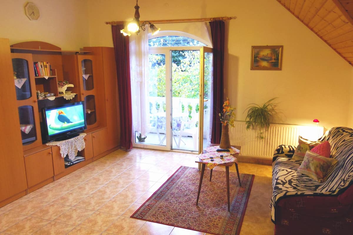 Een woonkamer met een televisie, een bank, een tafel met een plant en een schuifdeur die uitkomt op een terras.