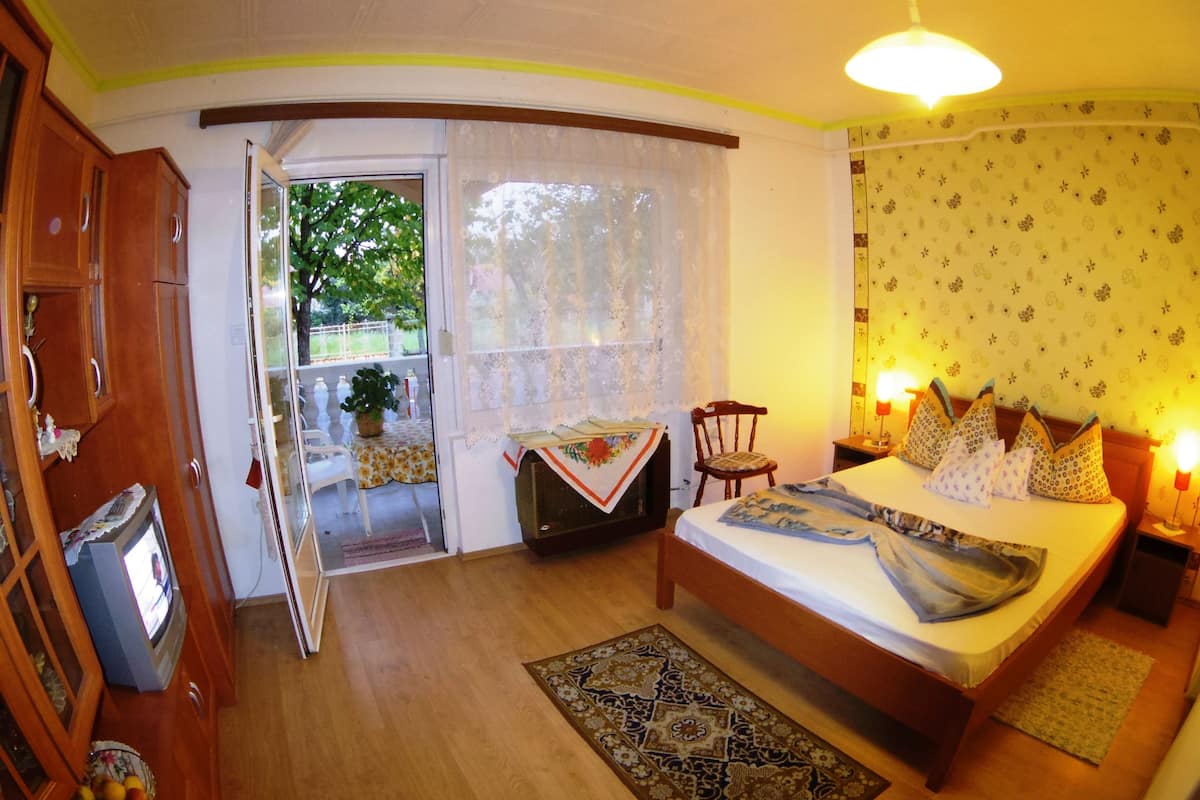 Een slaapkamer met een bed, nachtkastjes, een raam met gordijnen, een kleine tafel met een stoel en een televisie.