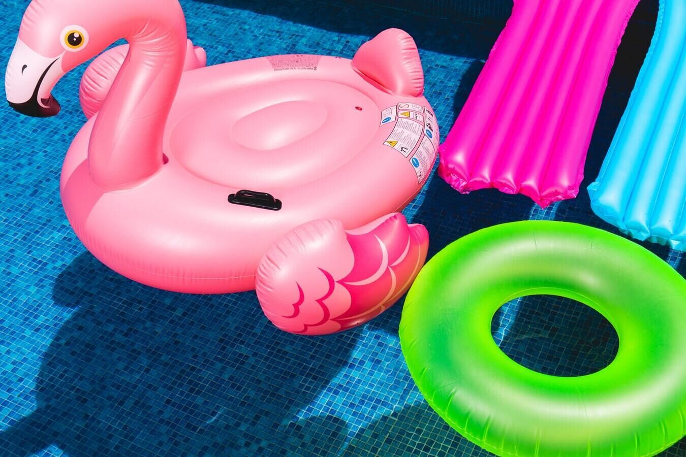 A pool with inflatable toys including a pink flamingo float and a green ring float.