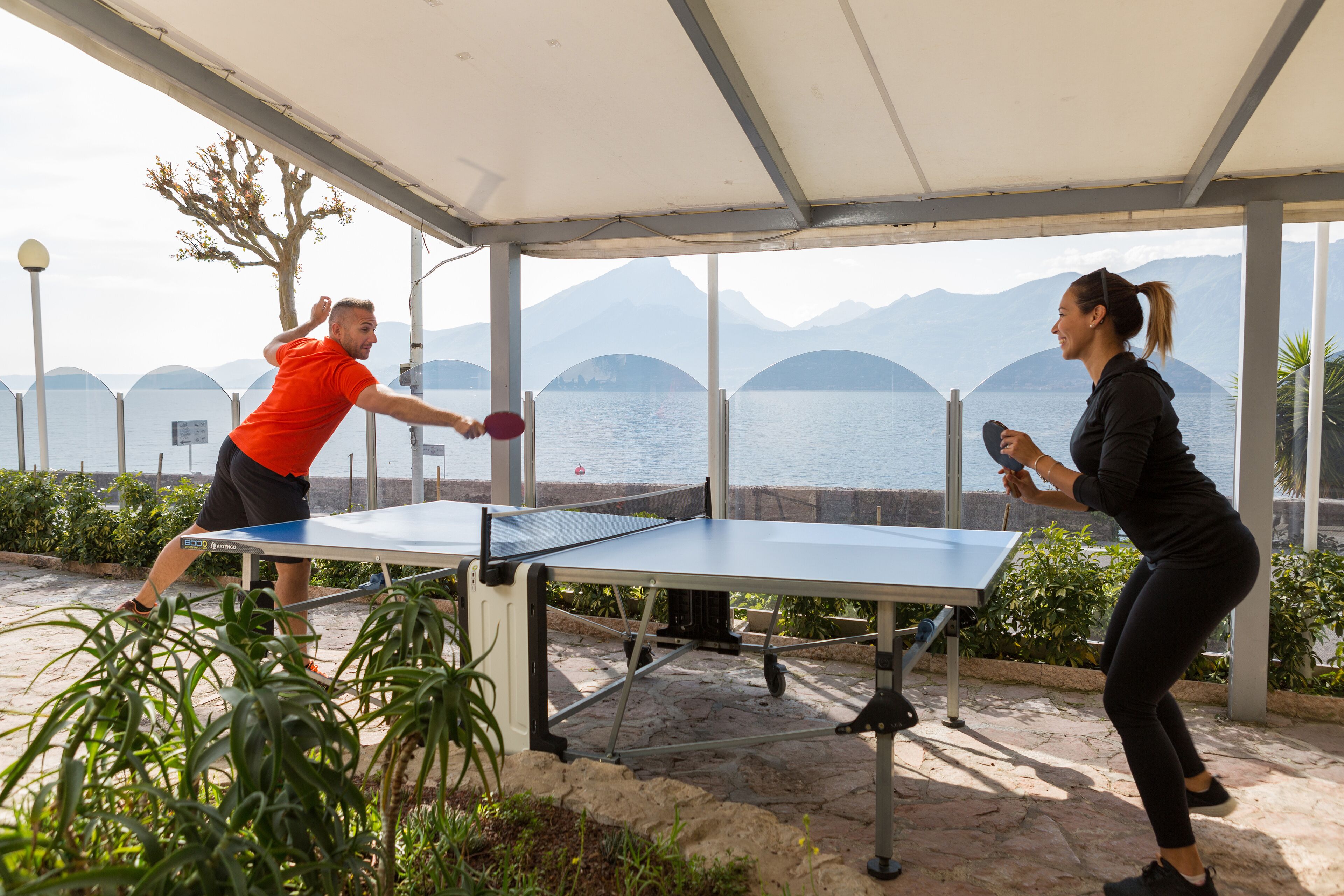 Een tafeltennistafel buiten opgesteld, met een schilderachtig meer en bergen op de achtergrond.