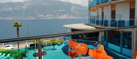 Een balkon met een tafel, een drankje en uitzicht op zee en bergen.