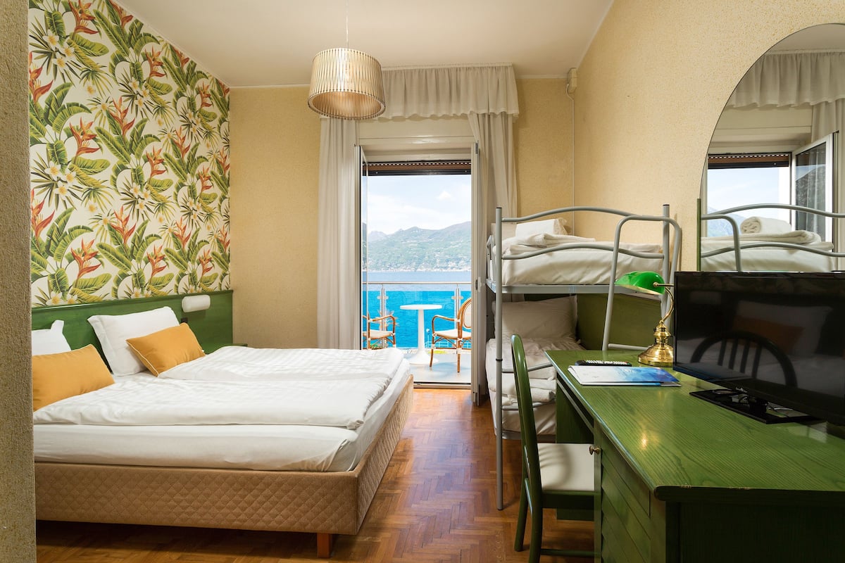 A room with a bed, bunk beds, a desk with a computer, and a view of the sea.