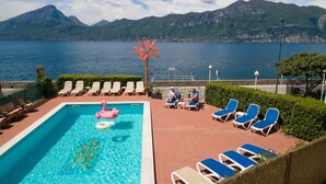 A pool area with lounge chairs, a pool, and a view of mountains and water. - Hotel Caribe by Double Hospitality (Brenzone sul Garda)