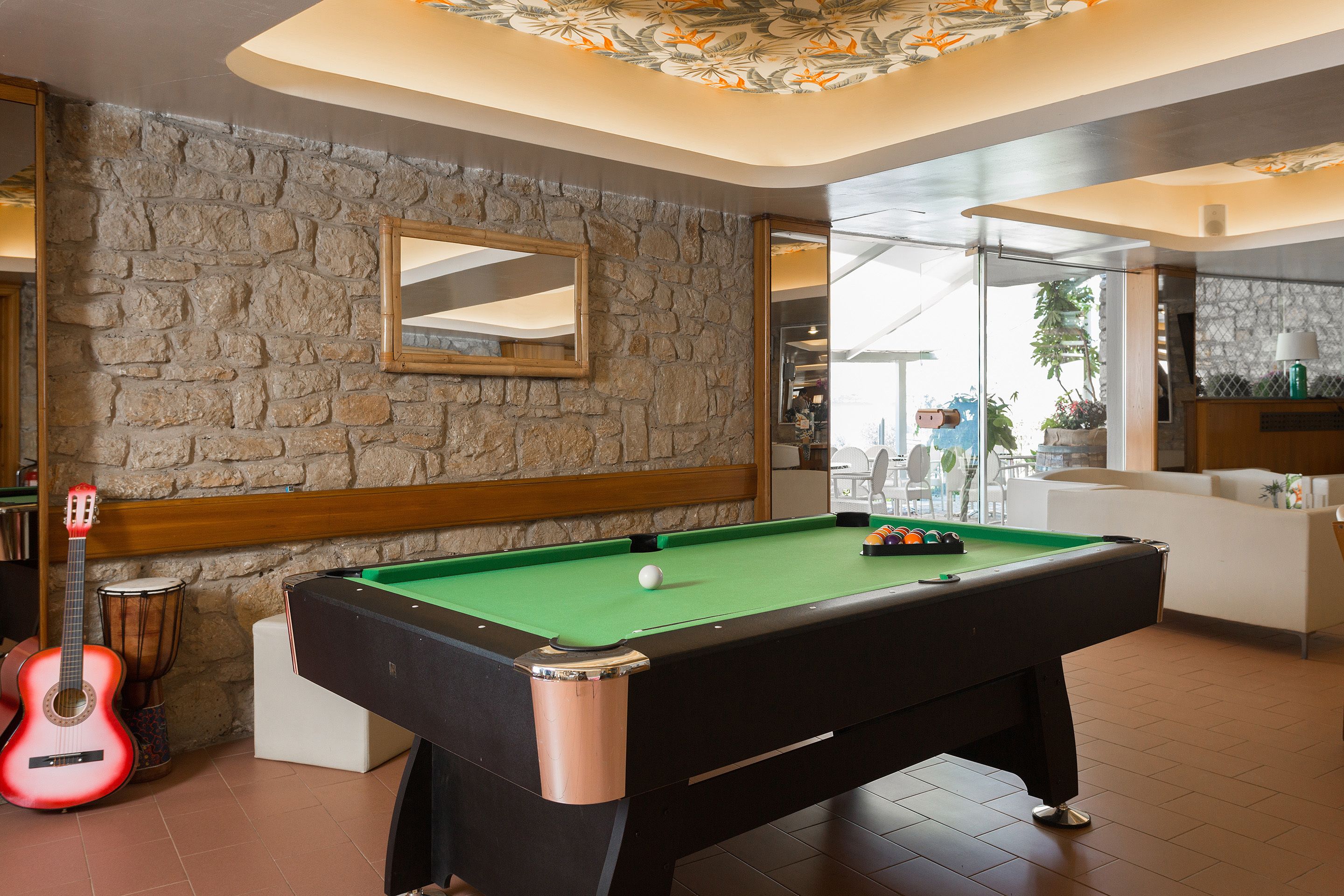 Een pooltafel met een groene viltkleed, houten rand en een spiegelwand erboven.