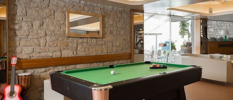 A pool table with a green felt surface, a wooden frame, and a mirrored wall above it.