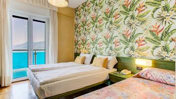 Ein Hotelzimmer mit zwei Betten, Meerblick durch eine Schiebetür und tropischer Tapete.