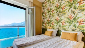 A hotel room with a bed, a view of the sea, and a tropical wallpaper. - Hotel Caribe by Double Hospitality (Brenzone sul Garda)