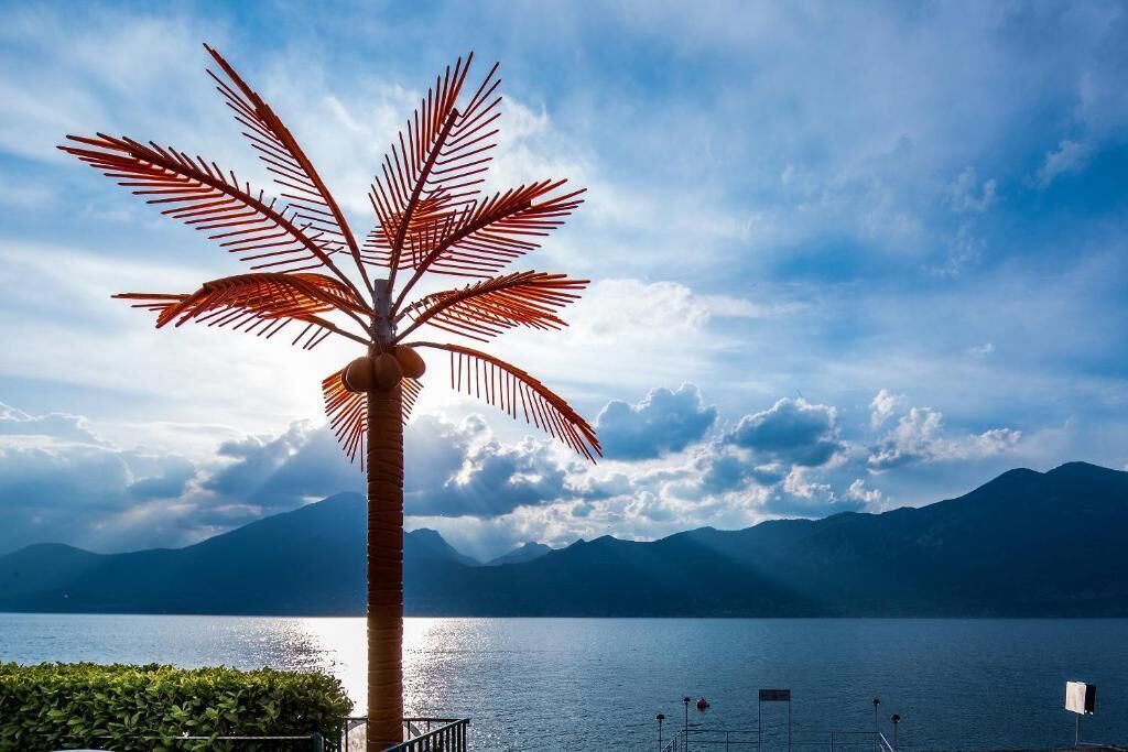 Una escultura de palmera frente a un lago con montañas al fondo.