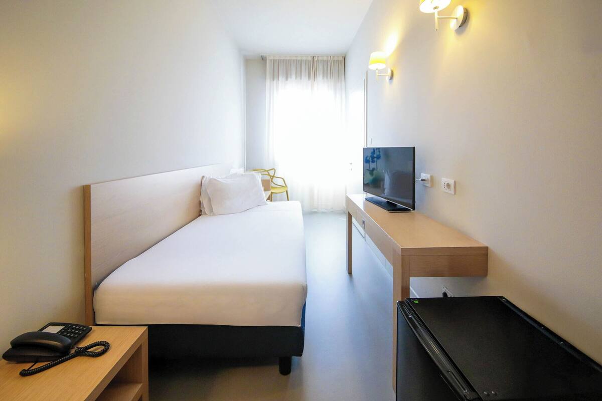 Ein Hotelzimmer mit einem Bett, einem Schreibtisch mit Fernseher, Telefon und einem Sessel.