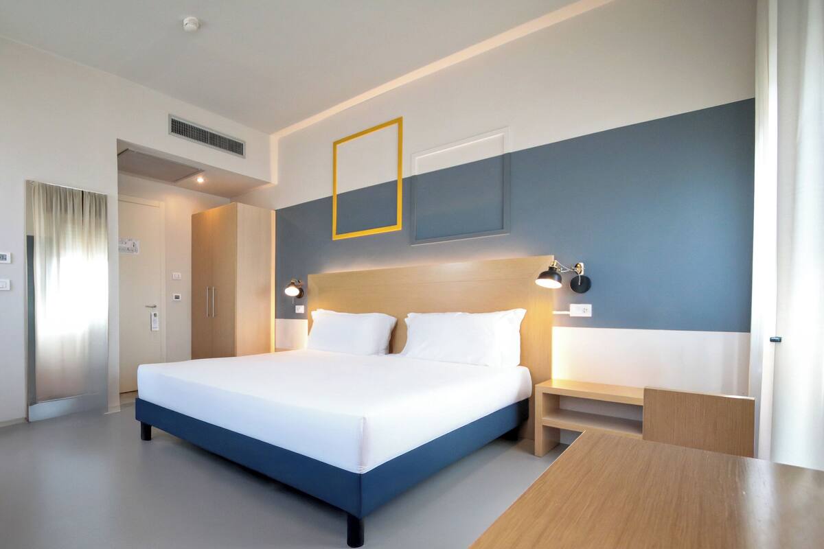 Ein modernes Hotelzimmer mit einem großen Bett, Nachttischen, einem Schreibtisch und einem an der Wand montierten Fernseher.