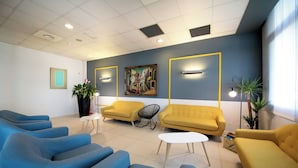 Un área de espera moderna con sofás azules y amarillos, una mesa blanca y un cuadro en la pared.